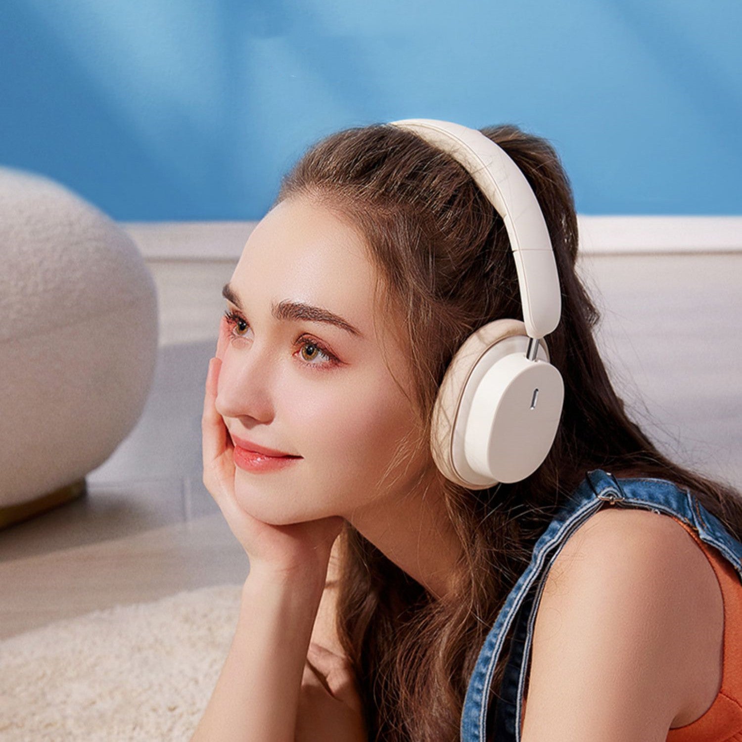 Woman wearing white headphones sitting on a couch with a blue wall in the background